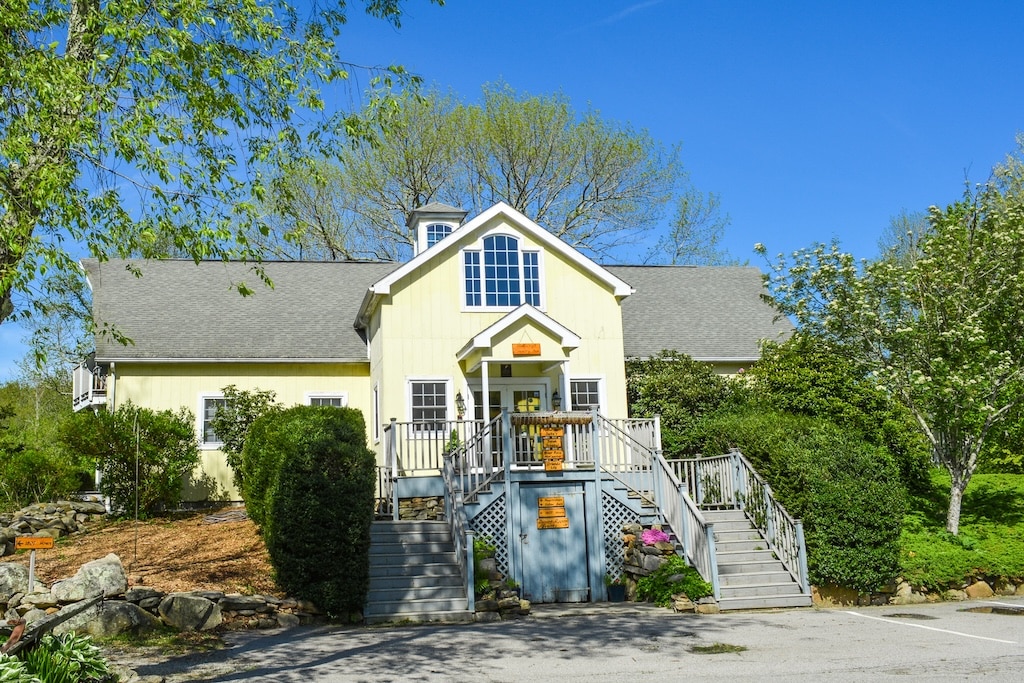 A yellow house with a central entrance and steps, surrounded by greenery and trees.